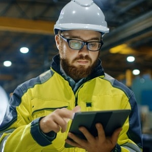 industrial engineer in a hard hat wearing safety jacket using tablet